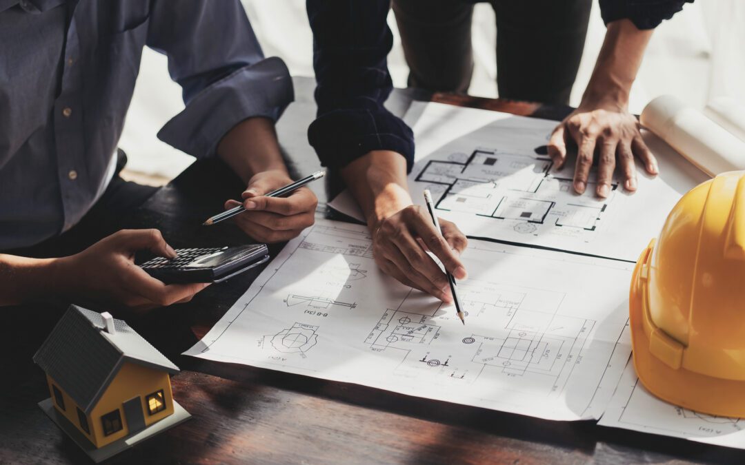 Hands reviewing architectural plans with yellow hard hat